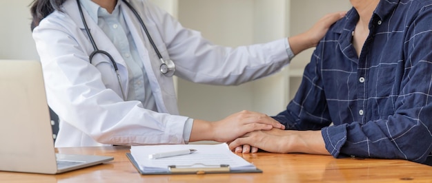 Médica alentando a un paciente masculino sosteniéndole la mano y golpeándole el hombro