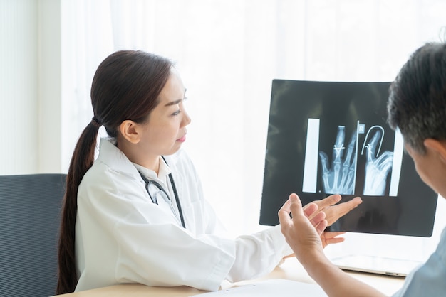 Médica asiática e paciente discutindo algo enquanto está sentado na mesa