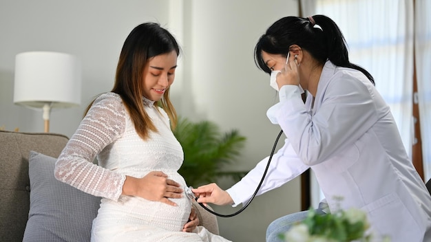 Médica asiática ou obstetra ouvindo os batimentos cardíacos do bebê pelo estetoscópio