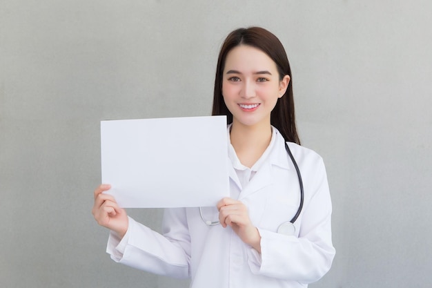 Médica asiática que usa jaleco segura e mostra um papel branco para apresentar algo