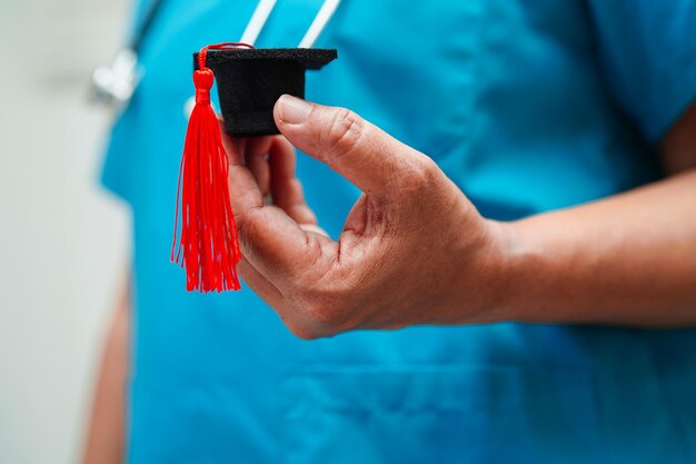 Médica asiática segurando chapéu de formatura no hospital Conceito de educação médica