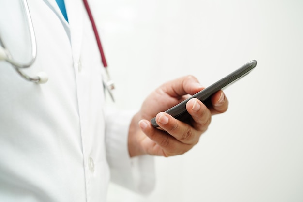 Médica asiática segurando telefone celular ou tablet para pesquisa de método de tratamento de paciente no hospital