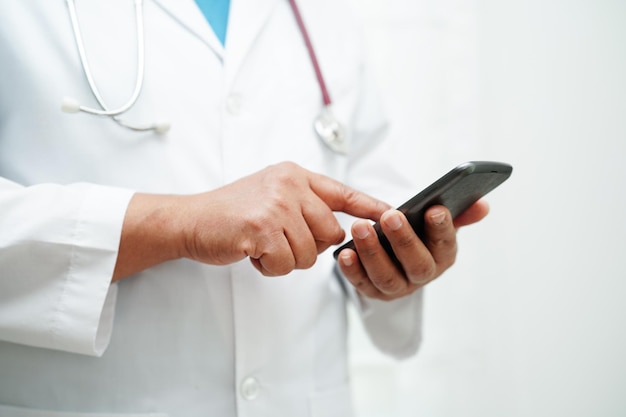 Médica asiática segurando telefone celular ou tablet para pesquisa de método de tratamento de paciente no hospital