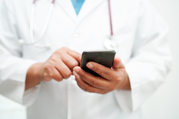 Médica asiática segurando telefone móvel ou tablet para pesquisar o método de tratamento do paciente no hospital