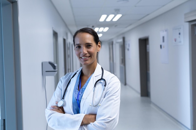 Médica con los brazos cruzados mirando a la cámara en el corredor del hospital