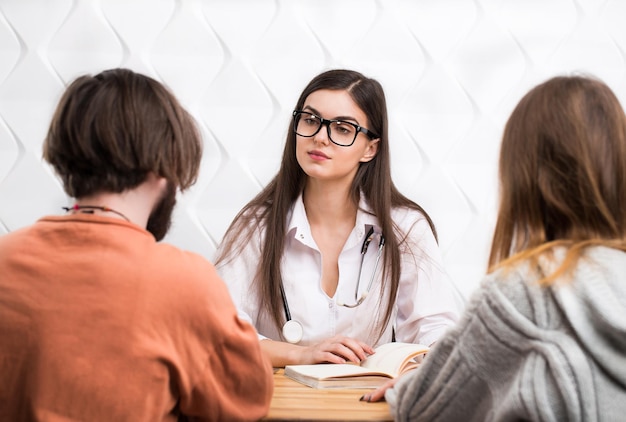 Médica caucasiana inteligente falando com um casal barbudo de cabelos escuros e mulher de cabelos compridos