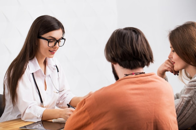 Médica caucasiana inteligente falando com um casal barbudo de cabelos escuros e mulher de cabelos compridos