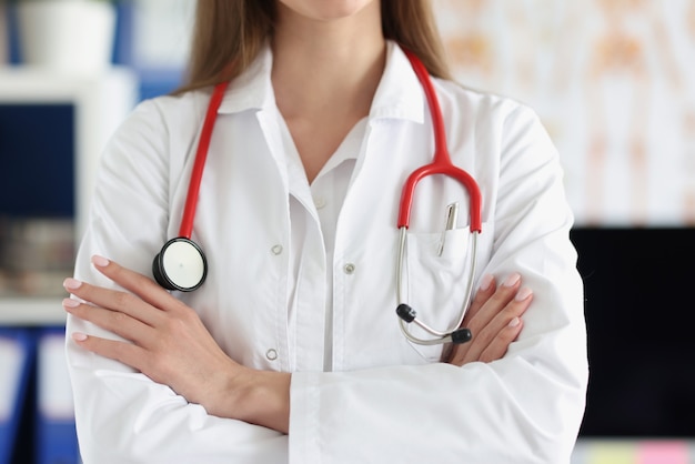 Médica com estetoscópio vermelho em pé de uniforme com as mãos postas closeup