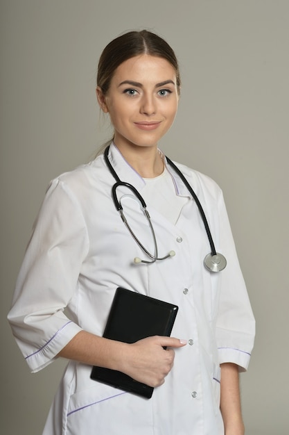 Médica com tablet pc, de pé sobre fundo cinza