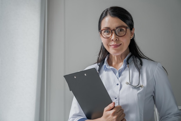 Médica confiante em pé no escritório e sorrindo para a câmera