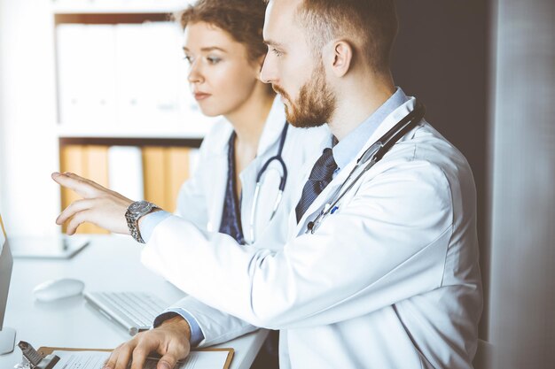 Foto médica de barba ruiva com uma colega discutindo a terapia atual da doença enquanto está sentada no local de trabalho na clínica ensolarada. trabalho em equipe na medicina.