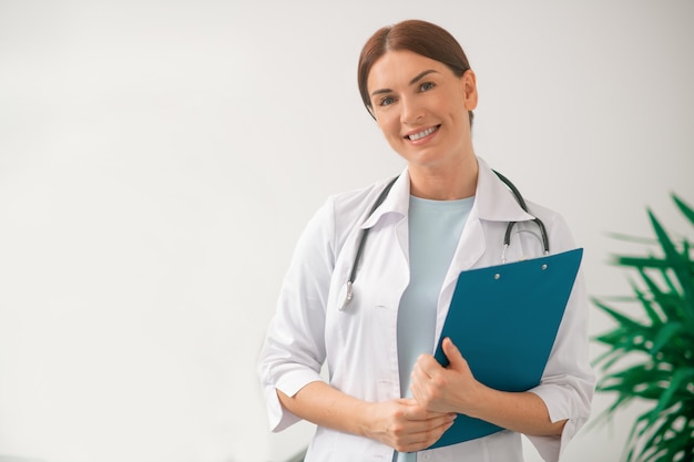 Médica de cabelos escuros e uma túnica branca sentada no consultório do médico