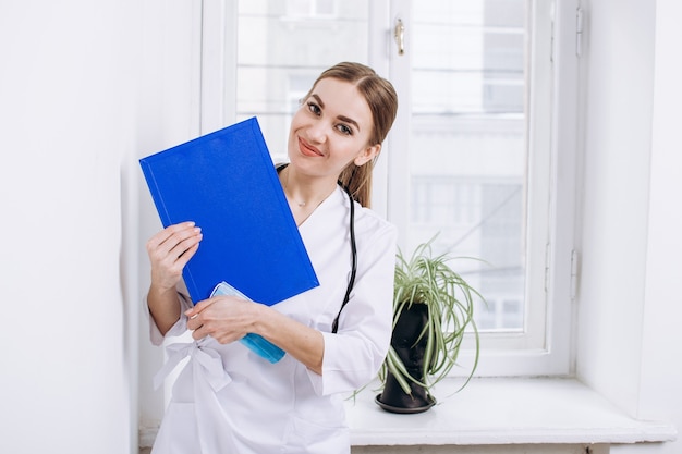 Médica de jaleco branco com estetoscópio e pasta azul