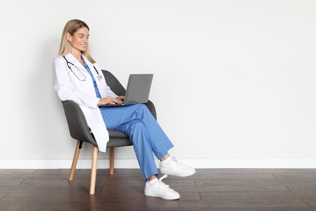 Foto médica de medicina moderna em uniforme sentado na cadeira e usando laptop