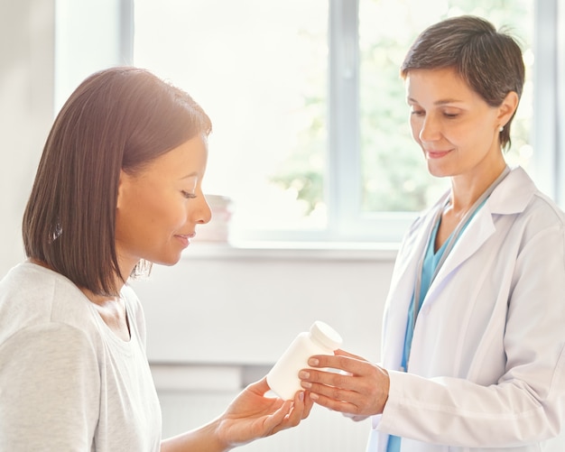 Médica de meia-idade sorridente, prescrevendo remédio e dando um frasco de vitaminas ao paciente