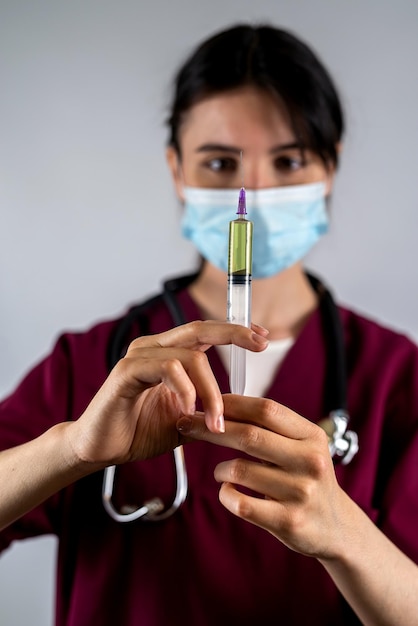 Médica de uniforme branco e luvas com uma seringa nas mãos posa para a câmera