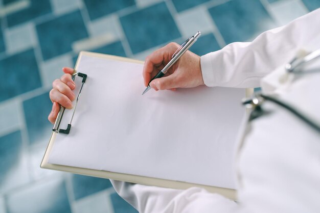 Foto médica de uniforme branco escrevendo em papel clipboard