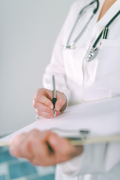 Foto médica de uniforme branco escrevendo em papel clipboard