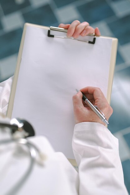 Foto médica de uniforme branco escrevendo em papel clipboard