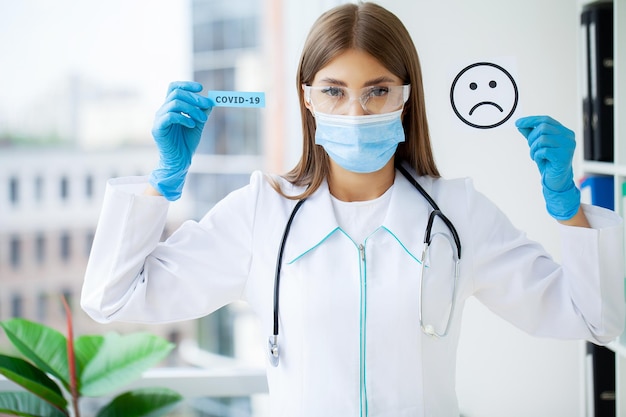 Médica de uniforme segurando uma placa de papel com letras covid