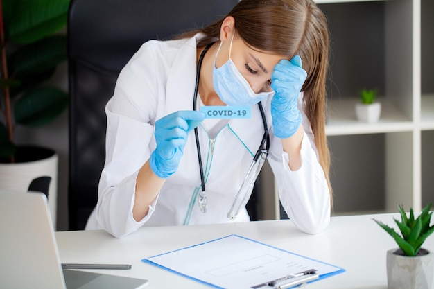 Médica de uniforme segurando uma placa de papel com letras covid