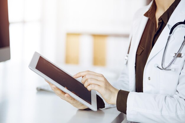 Médica desconhecida usando computador tablet na clínica ensolarada Conceito de medicina