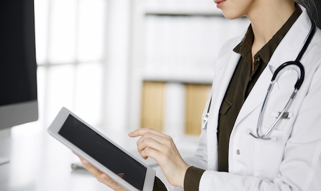 Médica desconhecida usando computador tablet na clínica. Serviço médico perfeito no hospital. Conceito de medicina.