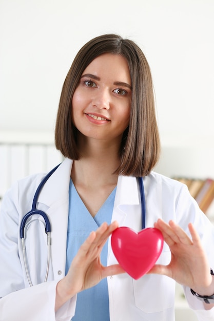 Médica em medicina feminina segurando um coração de brinquedo vermelho nas mãos