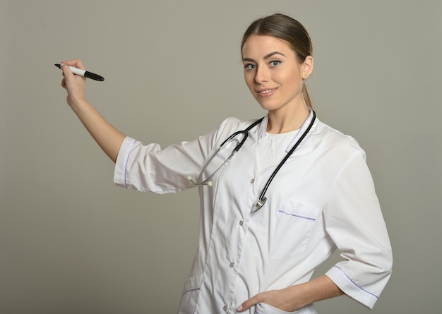 Médica em pé com uma caneta de feltro sobre fundo cinza