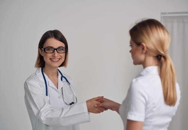 Médica em um vestido médico aperta a mão de um paciente em uma camiseta branca sobre um fundo claro