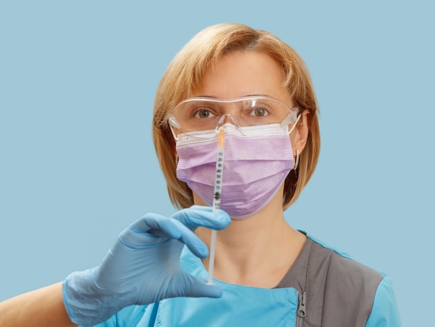 Médica em uma máscara de óculos e luvas segurando uma seringa com remédio líquido para injeção