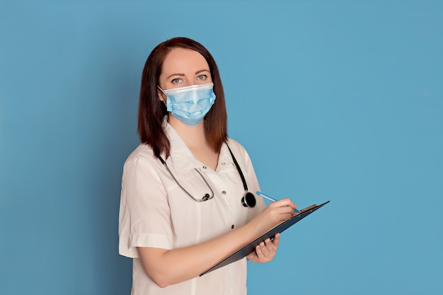 Médica em uma máscara médica com um estetoscópio escreve em um tablet. Conceito de saúde