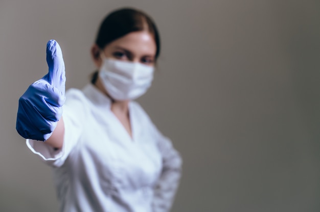 Foto médica em vestido de medicina e as luvas médicas na mão está mostrando um polegar para cima gesto