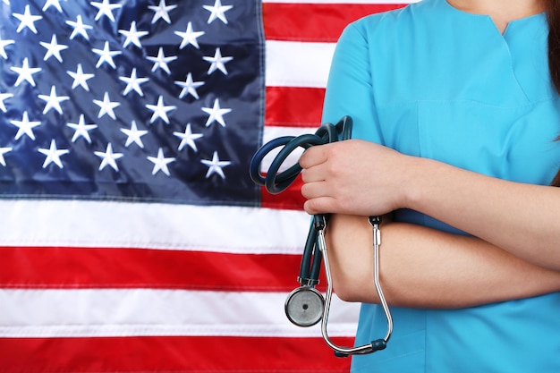 Foto médica con un estetoscopio en la mano con la bandera de los estados unidos en el fondo