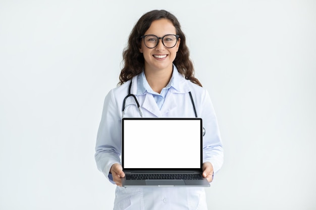 Médica europeia alegre segurando um laptop com tela branca