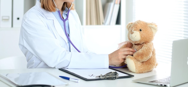 Médica examinando um paciente de ursinho de pelúcia pelo estetoscópio. Conceito de cuidados médicos para crianças