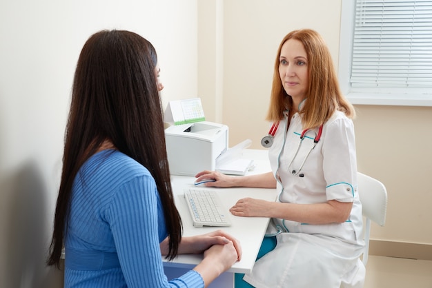 Foto médica falando com jovem paciente sentada em uma mesa no escritório