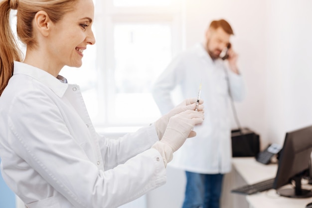 Médica feliz e encantada segurando uma seringa e sorrindo enquanto se prepara para fazer uma injeção