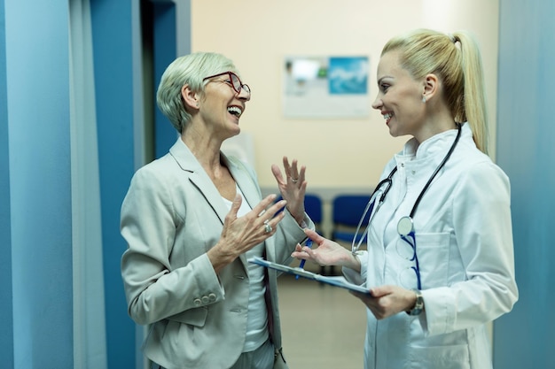 Foto médica feliz e mulher madura falando enquanto passa por relatórios médicos na clínica