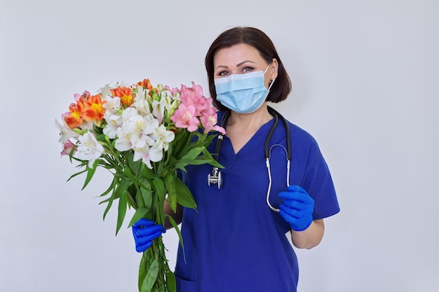 Médica feminina com máscara médica uniforme azul com buquê de flores sobre fundo claro