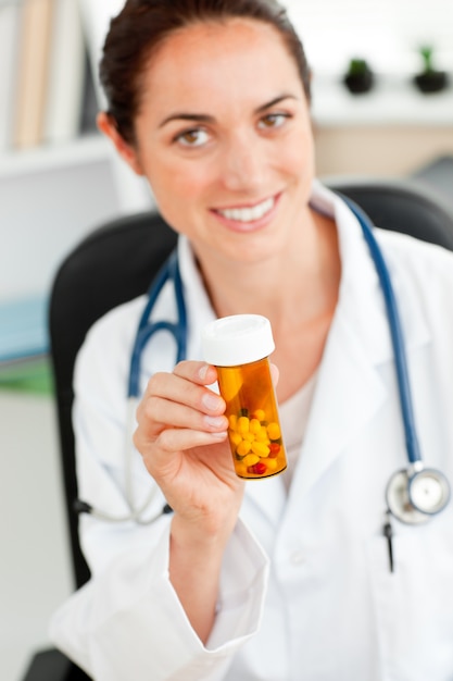 Médica feminina encantada segurando pílulas na câmera em seu escritório