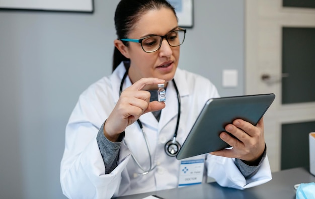 Médica haciendo consulta en línea con una tableta que muestra la vacuna contra la COVID-19