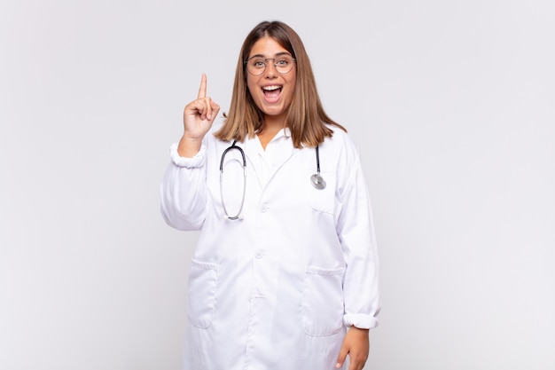 Médica jovem sentindo-se um gênio feliz e animado depois de realizar uma ideia, levantando o dedo alegremente, eureka!