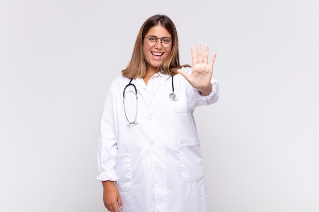 Médica jovem sorrindo e parecendo amigável, mostrando o número cinco ou quinto com a mão para a frente, em contagem regressiva