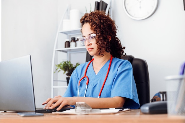 Médica latina com óculos usando um laptop em seu escritório