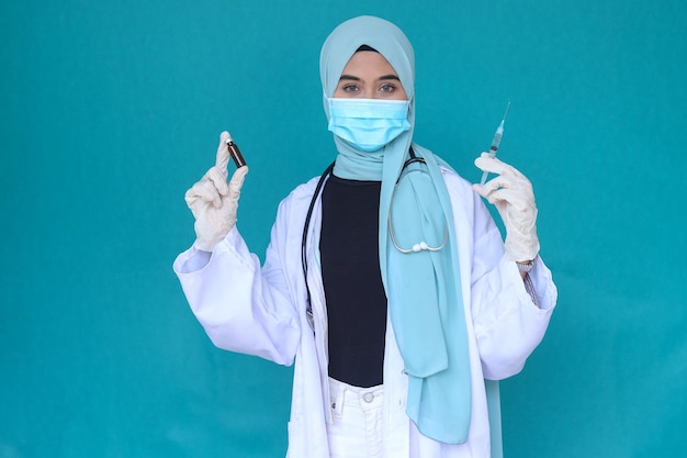 Médica muçulmana em hijab usando luvas protetoras e máscara médica segurando a seringa de injeção w