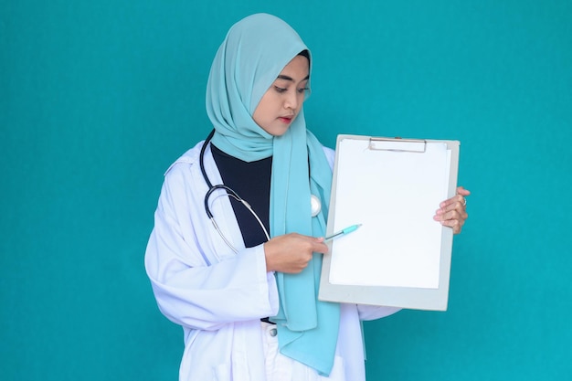 Médica muçulmana usando hijab enquanto aponta para a área de transferência em branco