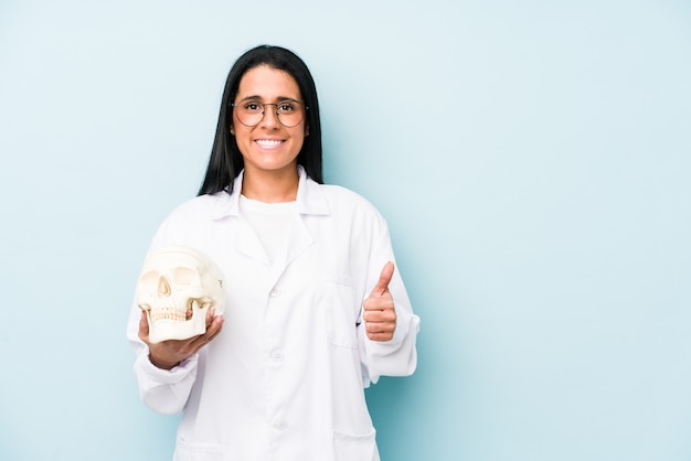 Médica mulher caucasiana isolada na parede azul sorrindo e levantando o polegar