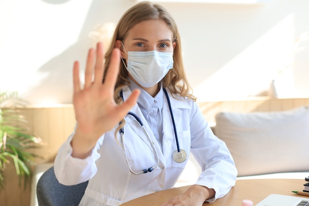 Médica na máscara facial, mostrando o sinal de stop com a mão.
