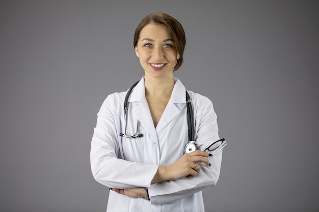 médica no jaleco branco. As mãos estão cruzadas no peito.